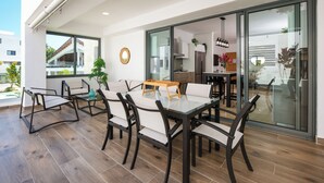 A modern dining area with a glass table and chairs, a kitchen visible through glass doors, and a view of the outside. - Amar'e Aparthotel & Spa (Las Terrenas)