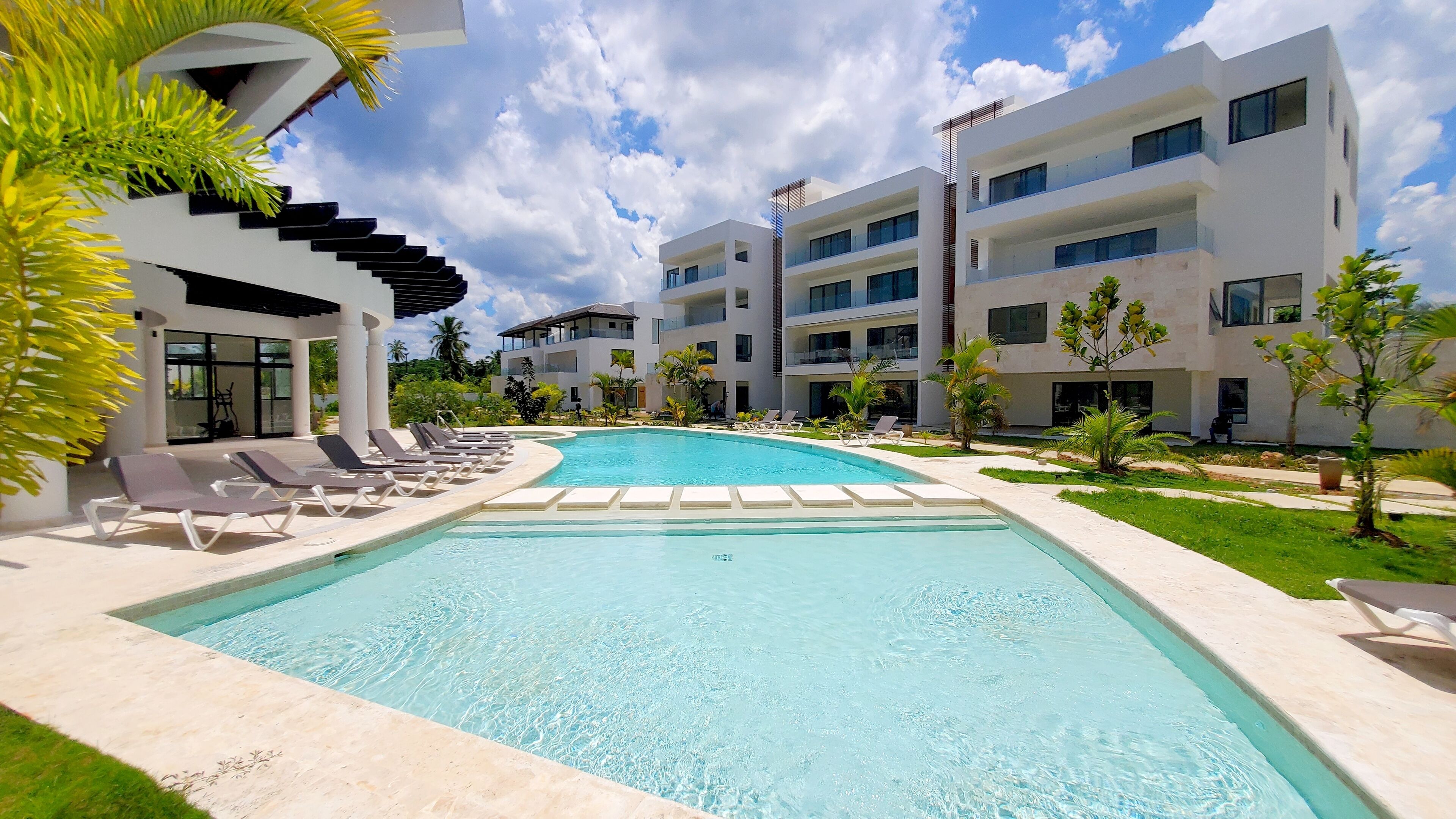 Ein modernes Resort mit einem zentral gelegenen Schwimmbad, Liegestühlen und einem gepflegten Garten.