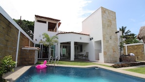 A swimming pool with a pink float, a covered patio, and a two-story building with a tiled roof.