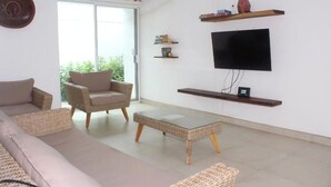 A modern living room with a sofa, armchair, and coffee table. There is a TV mounted on the wall and a sliding glass door leading to a balcony.