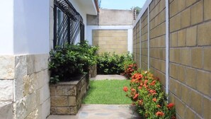 A narrow courtyard with a small lawn, stone planters with greenery, and a brick wall.