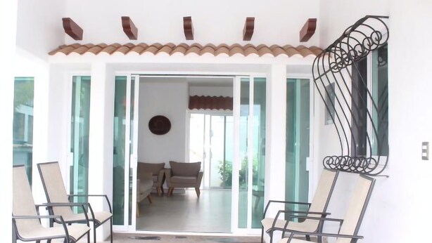 A room with a glass door leading to a living area, two chairs, a patterned floor, and a decorative metal railing.