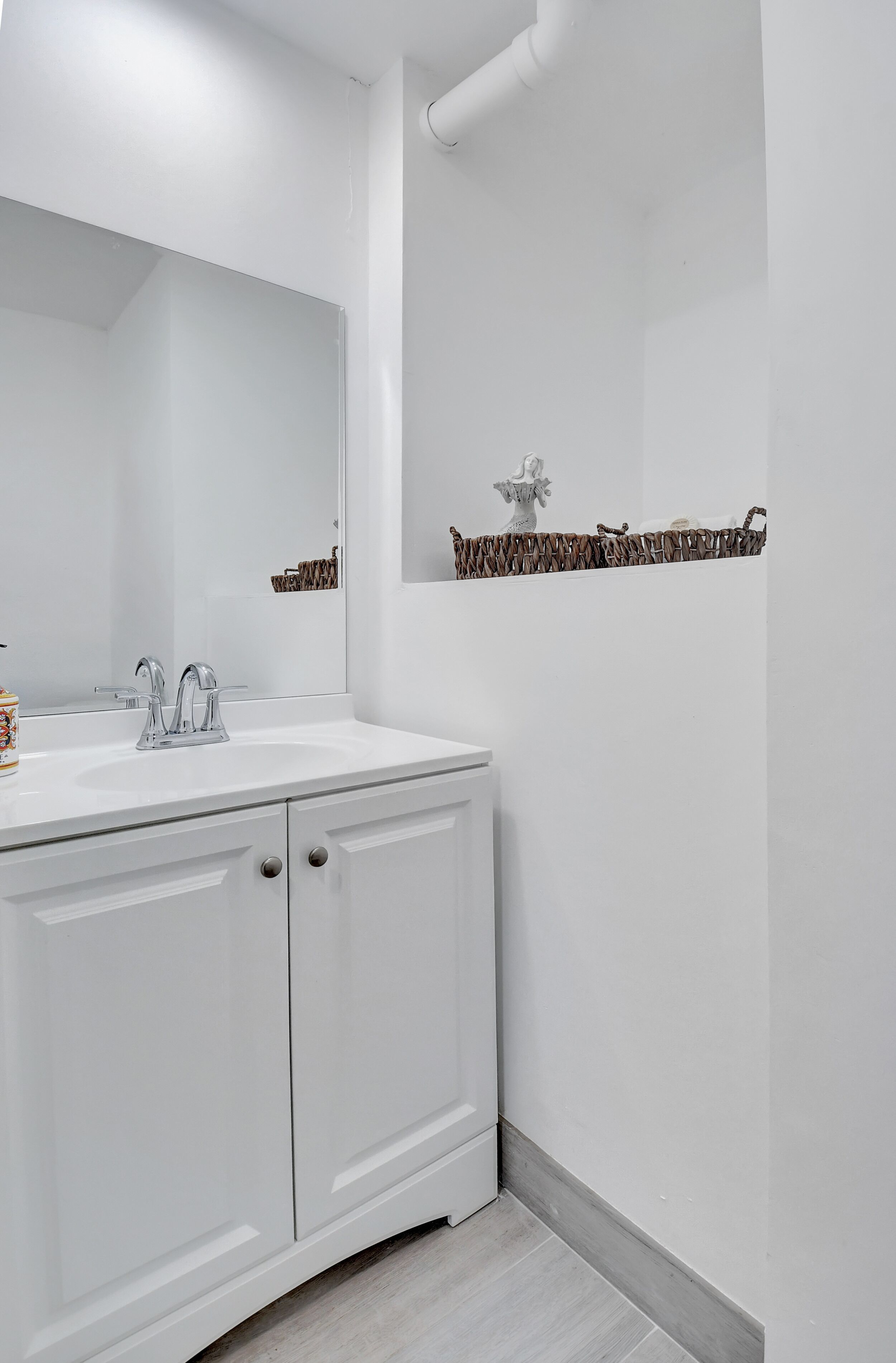 A modern bathroom with a white vanity, a large mirror, and a decorative shelf above the sink.