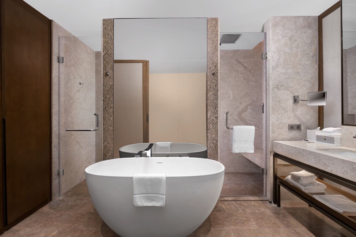 Un baño moderno con una bañera independiente grande, un lavabo redondo y un espejo sobre el lavabo.