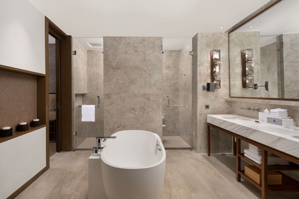 Un baño moderno con una bañera independiente, un espejo grande y un box de ducha de mármol.