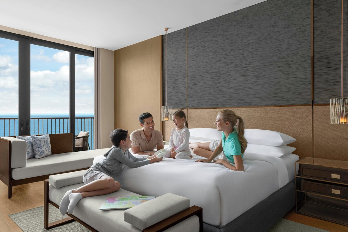 Una habitación de hotel moderna con una cama grande, un sofá y un balcón con vistas al mar.