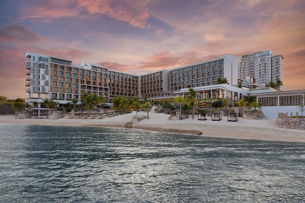 Un hotel con varias plantas, ubicación frente a la playa y zona de piscina.