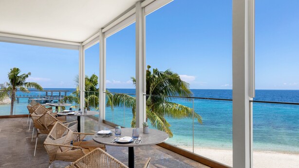 A sunlit outdoor dining area with wicker chairs and tables, overlooking a beach and turquoise sea. - Sheraton Cebu Mactan Resort (Lapu-Lapu)