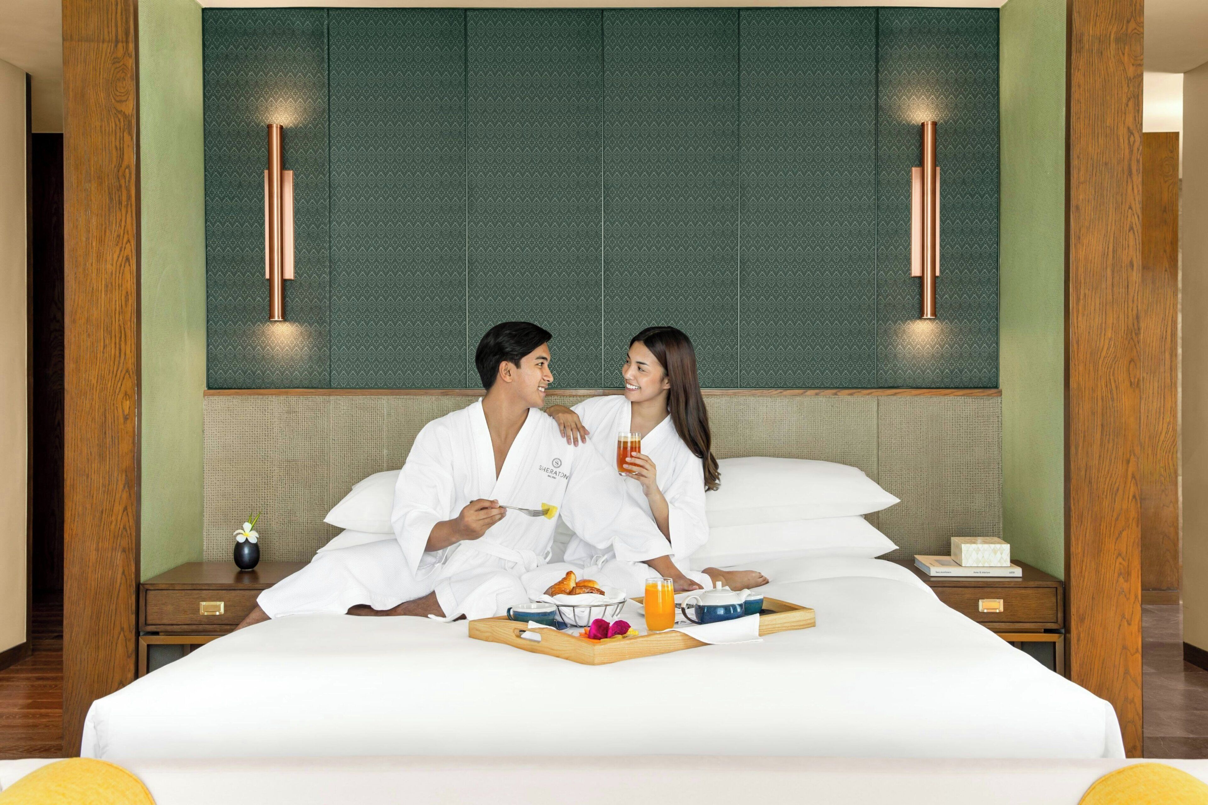 A hotel room with a large bed, a bedside table with a vase of flowers, and a tray with breakfast items.