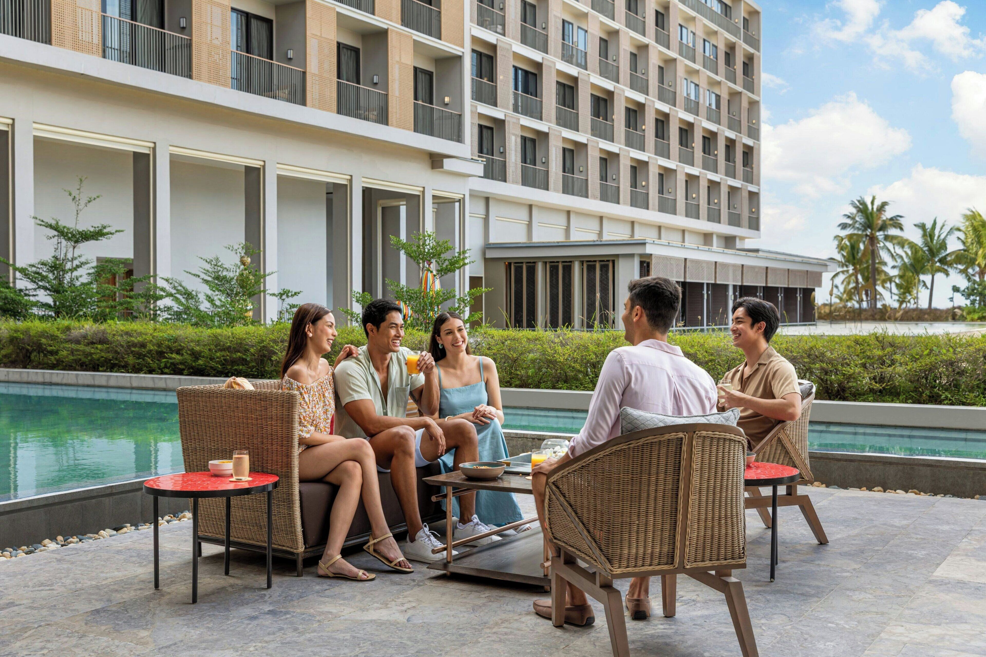 A group of people sitting around a table by a poolside, with a modern building in the background.