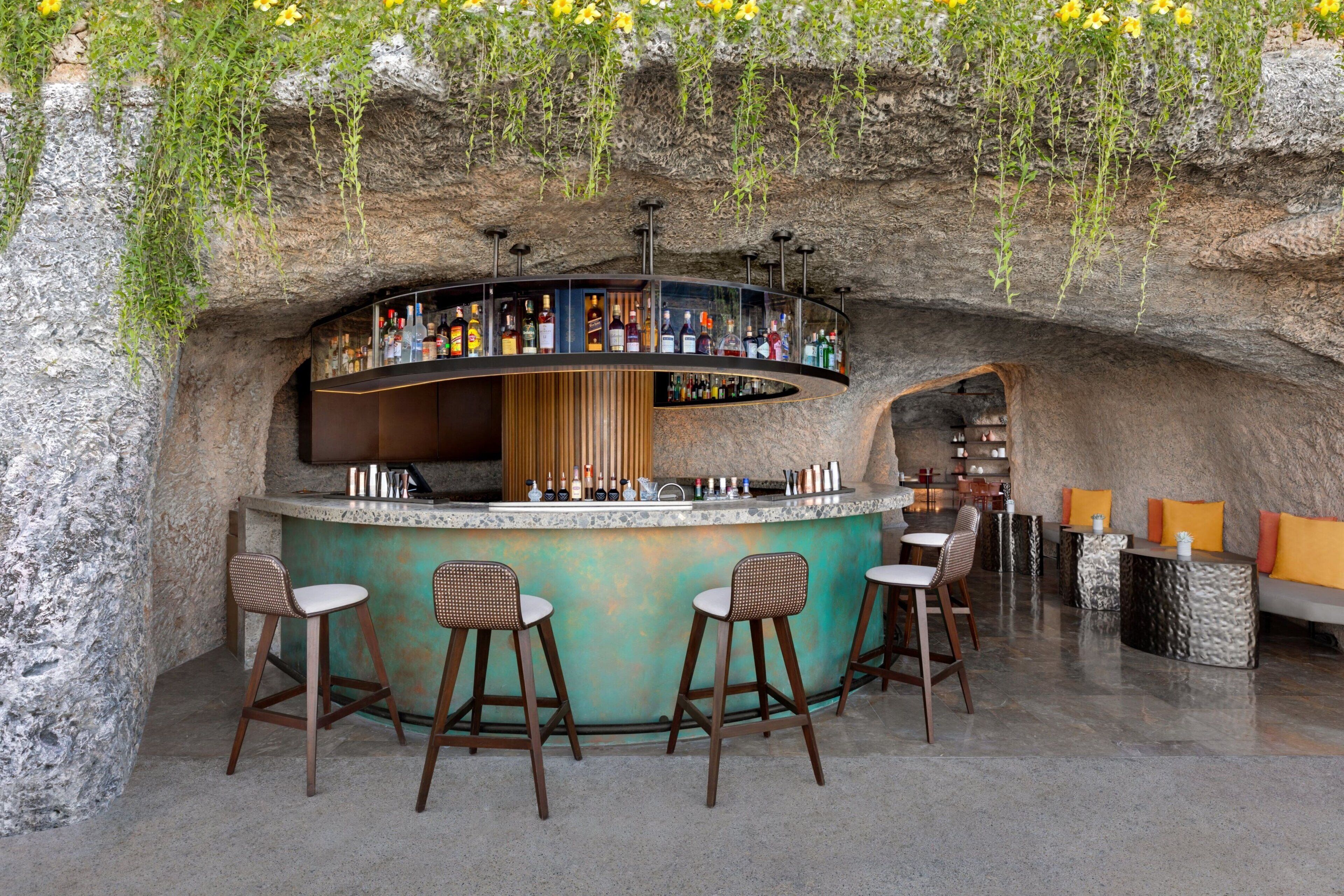 A bar with a curved counter, wooden stools, and a seating area with cushions.