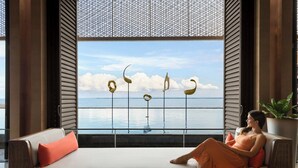 A modern living room with a large window overlooking a body of water, a sofa with a cushion, a tray with a book and a glass of orange juice, and a potted plant. - Sheraton Cebu Mactan Resort (Lapu-Lapu)