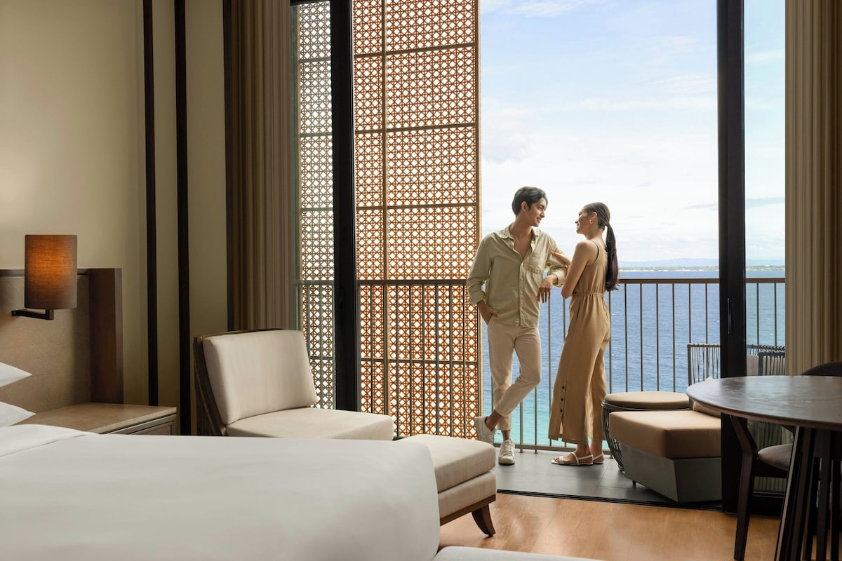 Habitación de hotel moderna con un ventanal grande, un balcón y vistas al mar.