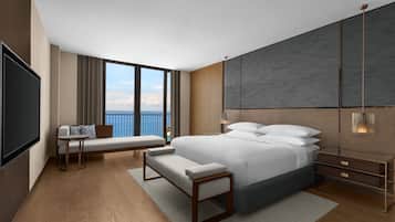 A modern hotel room with a large bed, a seating area with a bench, a small table, and a TV.
