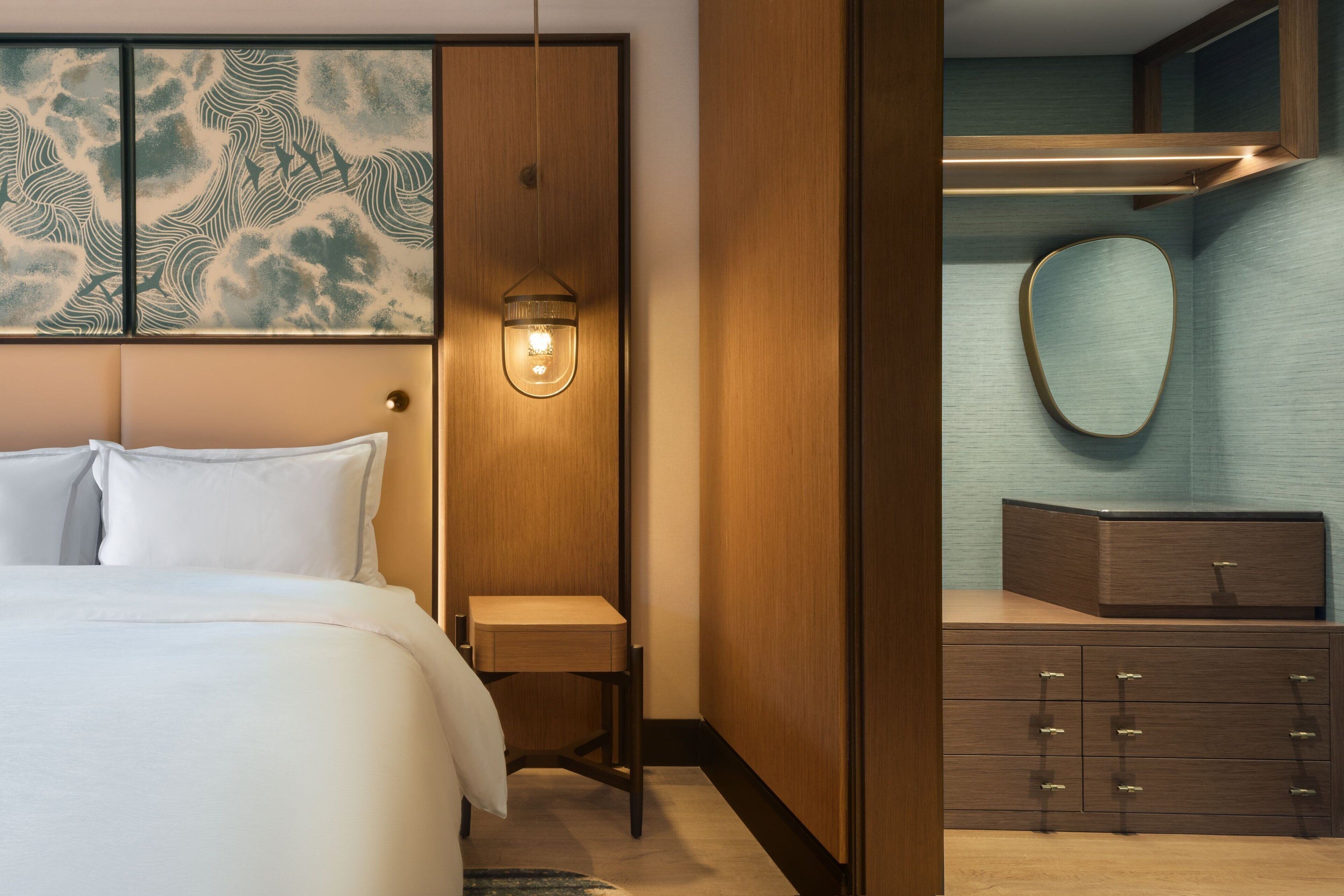 A hotel room with a bed, bedside table, and a mirror.