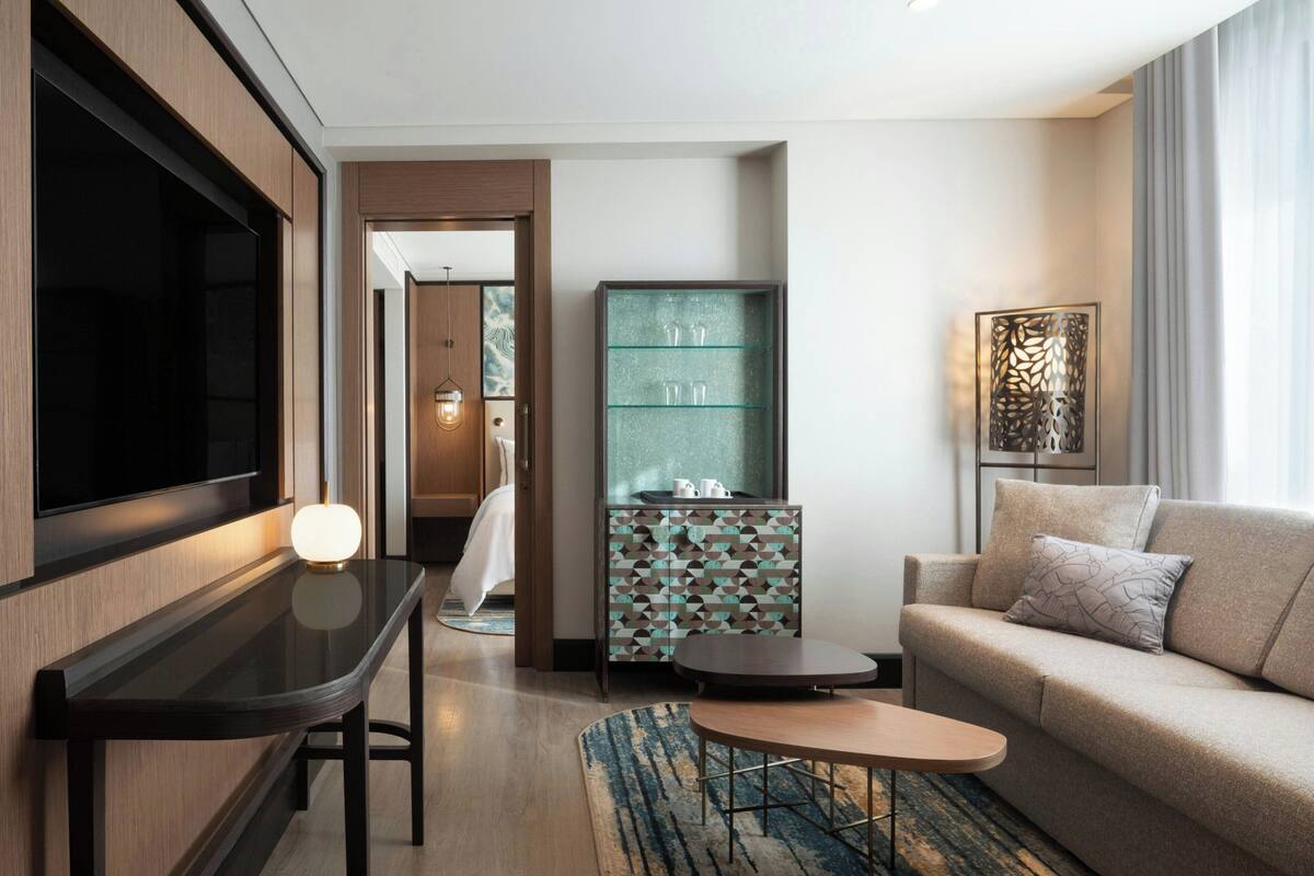 Une chambre d’hôtel moderne équipée d’un téléviseur à écran plat, d’une table basse en verre, d’un canapé et d’un meuble décoratif.