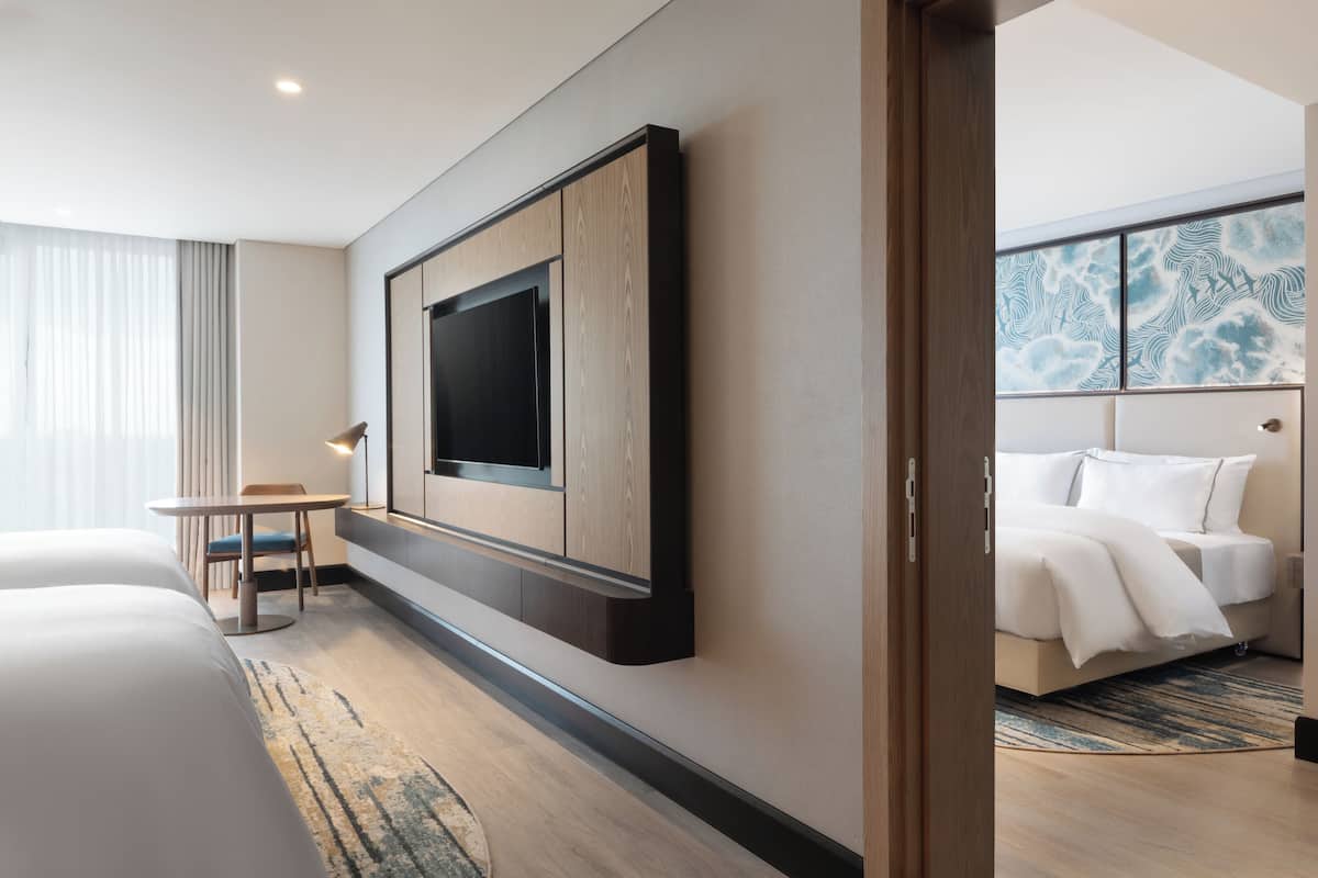 Una habitación de hotel moderna con una cama grande, un televisor de pantalla plana en la pared, una mesita con una silla y vistas al cielo a través de la ventana.