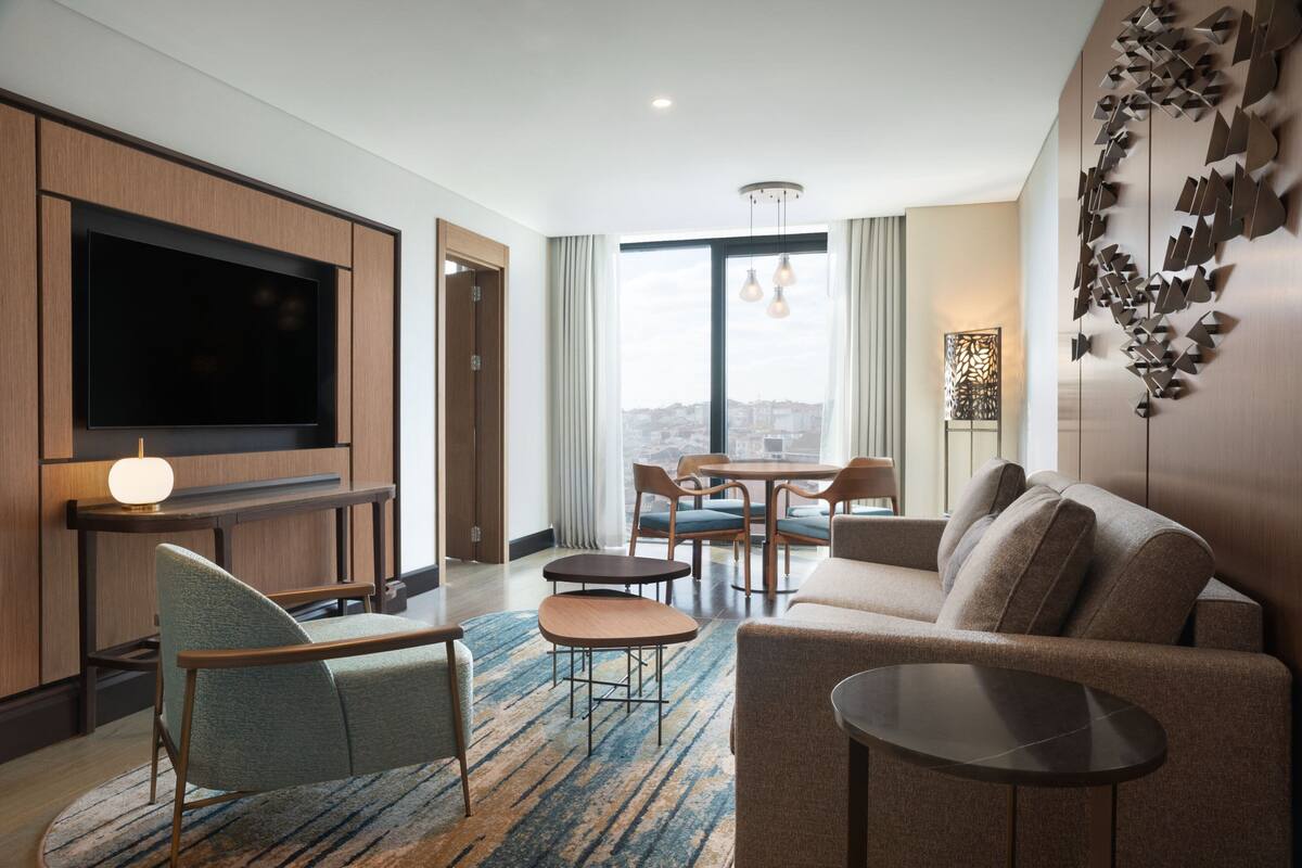 Une chambre d’hôtel moderne équipée d’un téléviseur à écran plat, d’un canapé, d’un fauteuil, d’une petite table et d’un coin repas avec des chaises et une table.