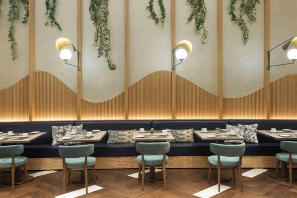 A restaurant interior with wooden paneling, green plants, and a seating area with tables and chairs.