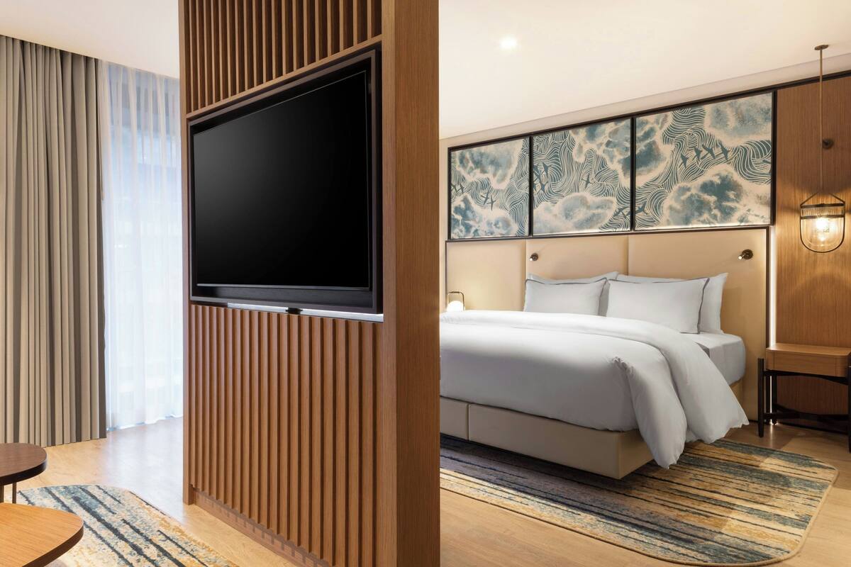 Une chambre d’hôtel moderne dotée d’un grand téléviseur à écran plat, d’un lit avec une literie blanche, d’un mur revêtu de panneaux en bois et d’une œuvre d’art décorative.