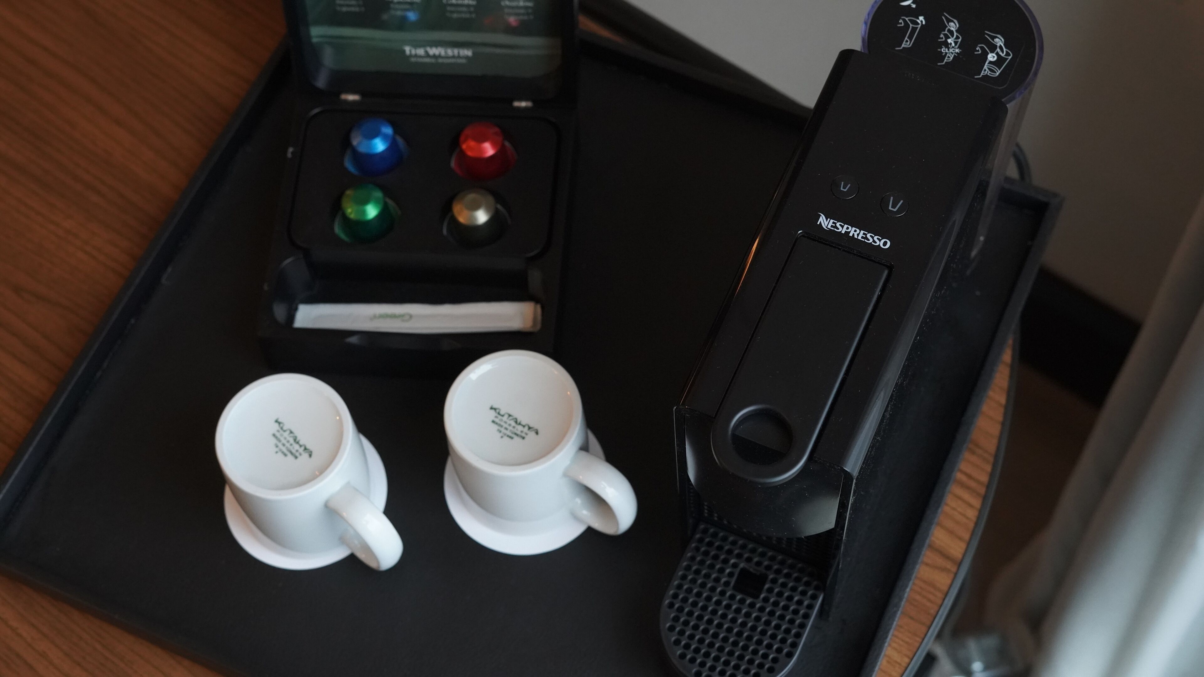 Een koffieapparaat met bedieningspaneel, twee witte kopjes en een zwart apparaat met het Nespresso logo.