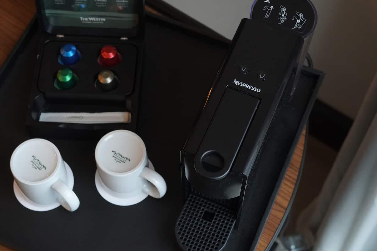 Una máquina de café con un panel de control, dos tazas blancas y un aparato negro con el logotipo de Nespresso.