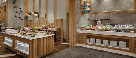 Un espace moderne dédié au buffet du petit-déjeuner, proposant une variété de plats, un coin café et un espace détente au design en bois.