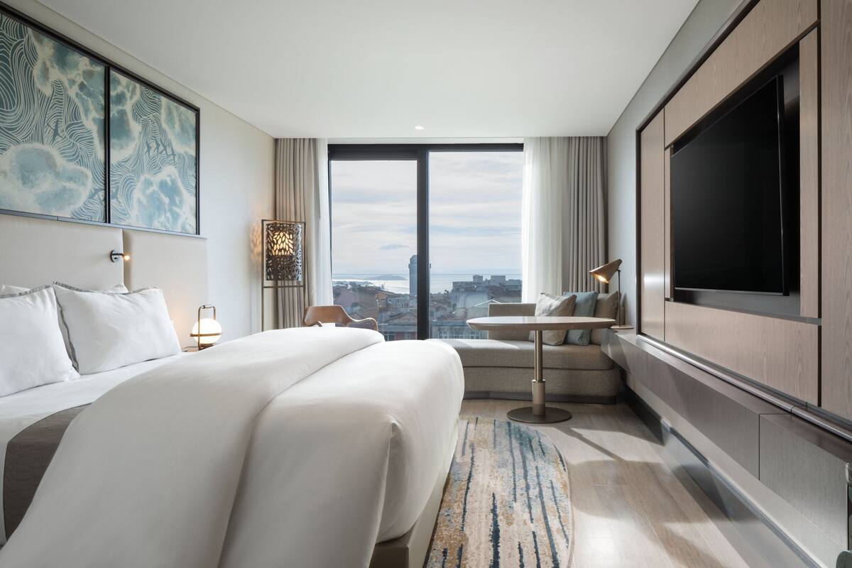 Une chambre d’hôtel moderne dotée d’un grand lit, d’un coin salon, d’une télévision à écran plat et offrant une vue sur la ville.