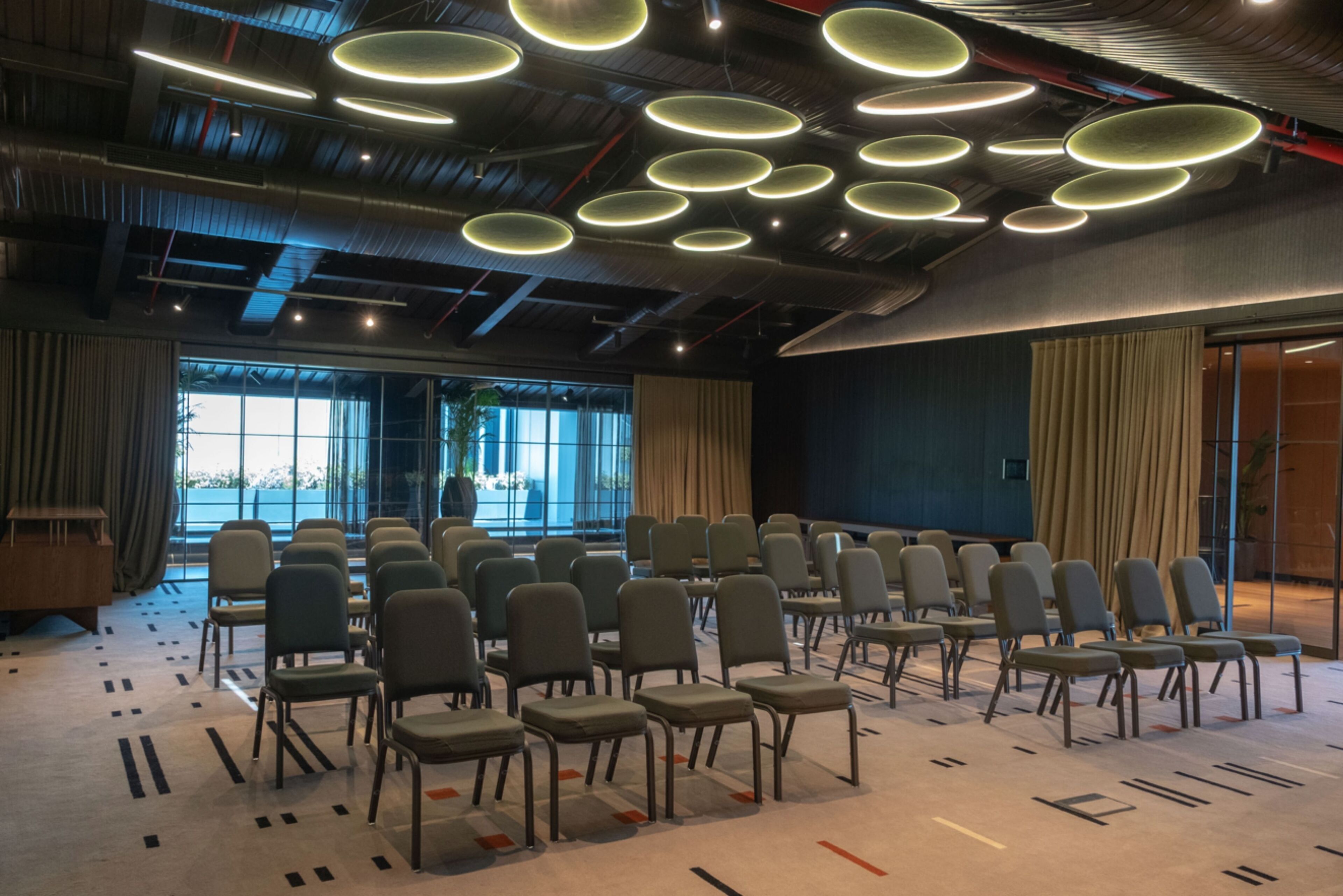 Ein Konferenzraum mit Stuhlreihen, einem gemusterten Teppich und modernen Deckenleuchten.
