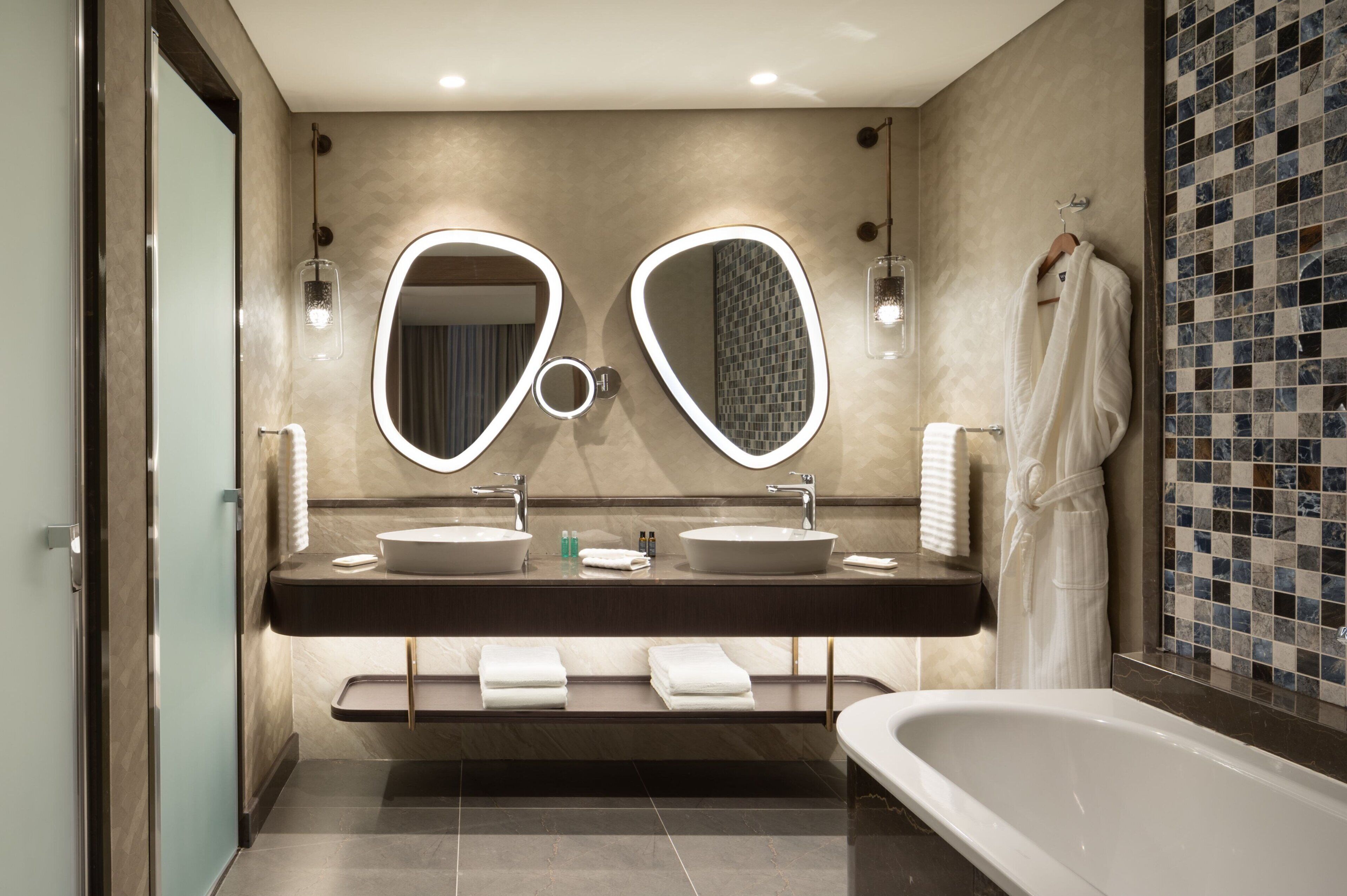 A modern bathroom with two sinks, a large mirror, and a bathtub.
