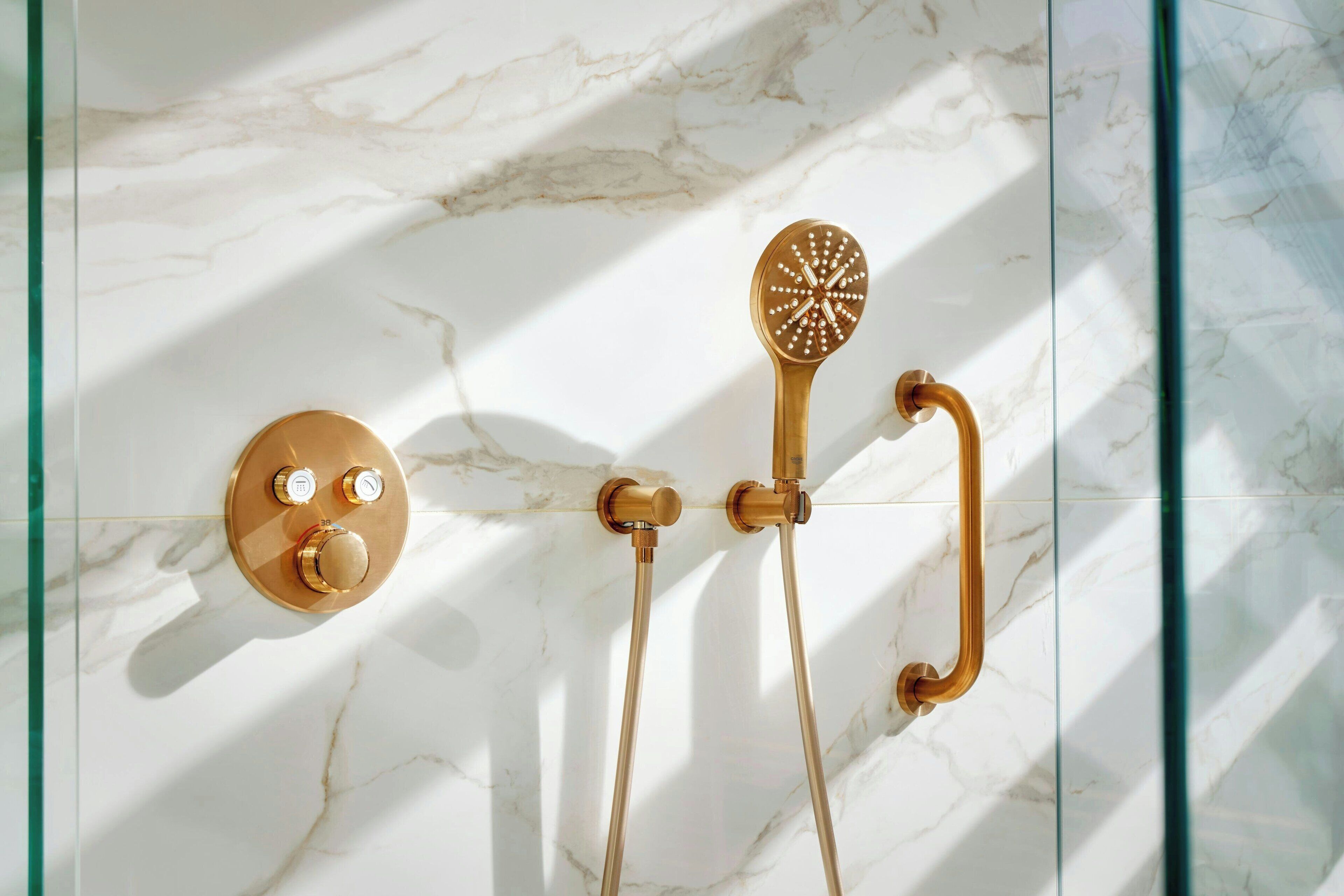A bathroom with a marble wall, a gold faucet, and a showerhead.