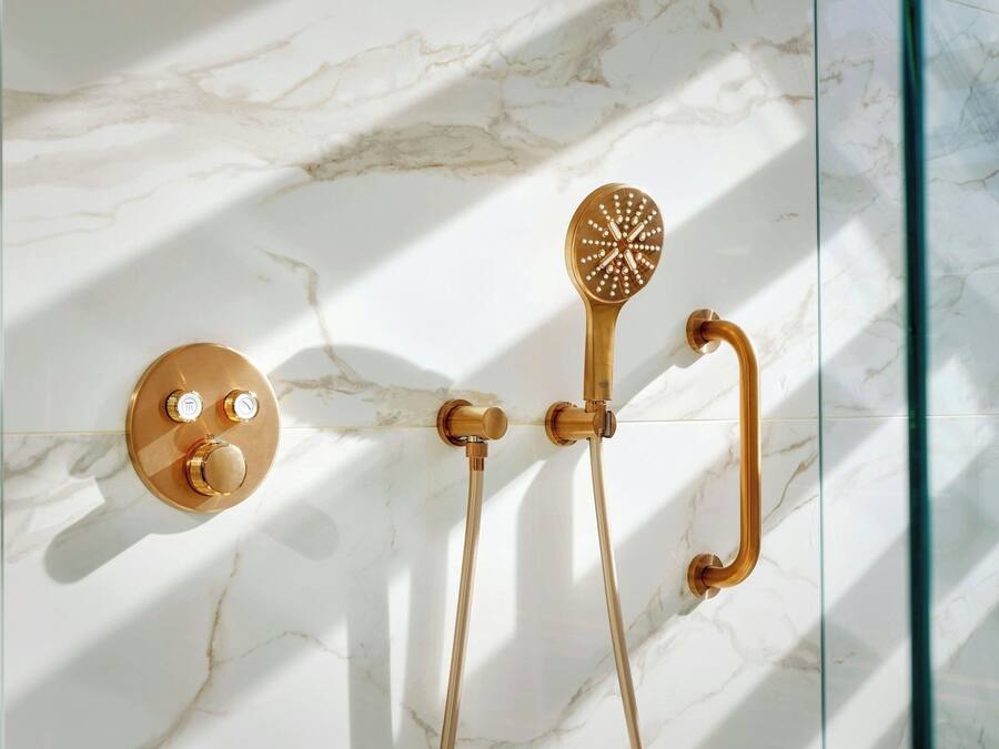 A bathroom with a marble wall, a gold faucet, and a showerhead.