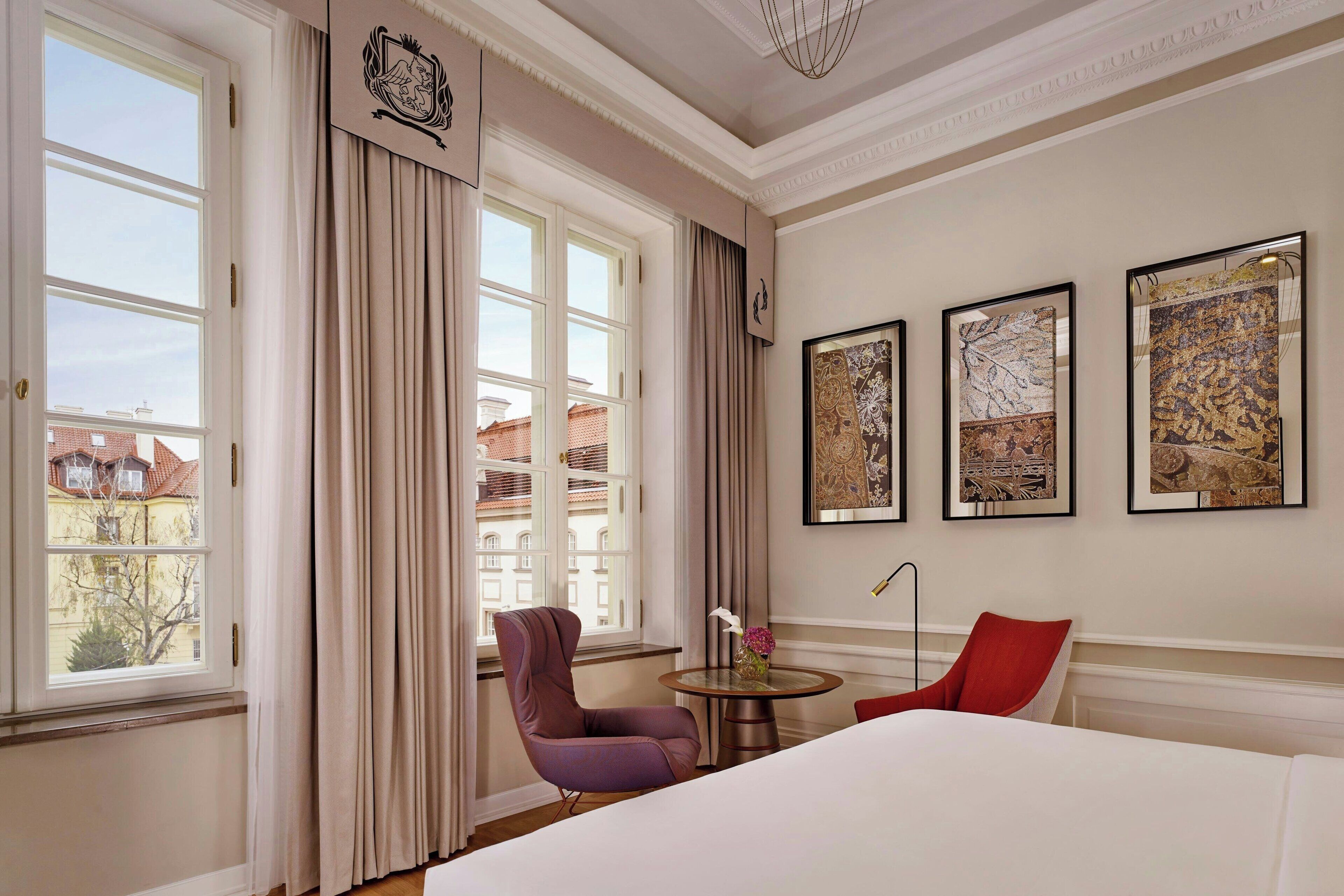 A hotel room with a large bed, a chair, a small table with a vase, and three framed pictures on the wall.