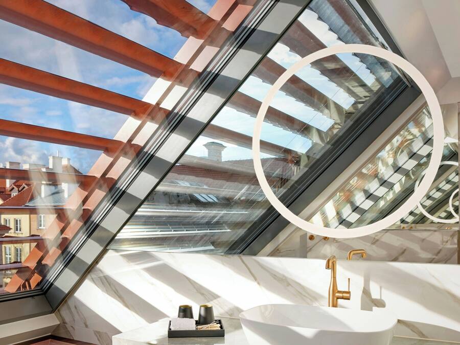 A modern bathroom with a skylight, a white sink, and a gold faucet.