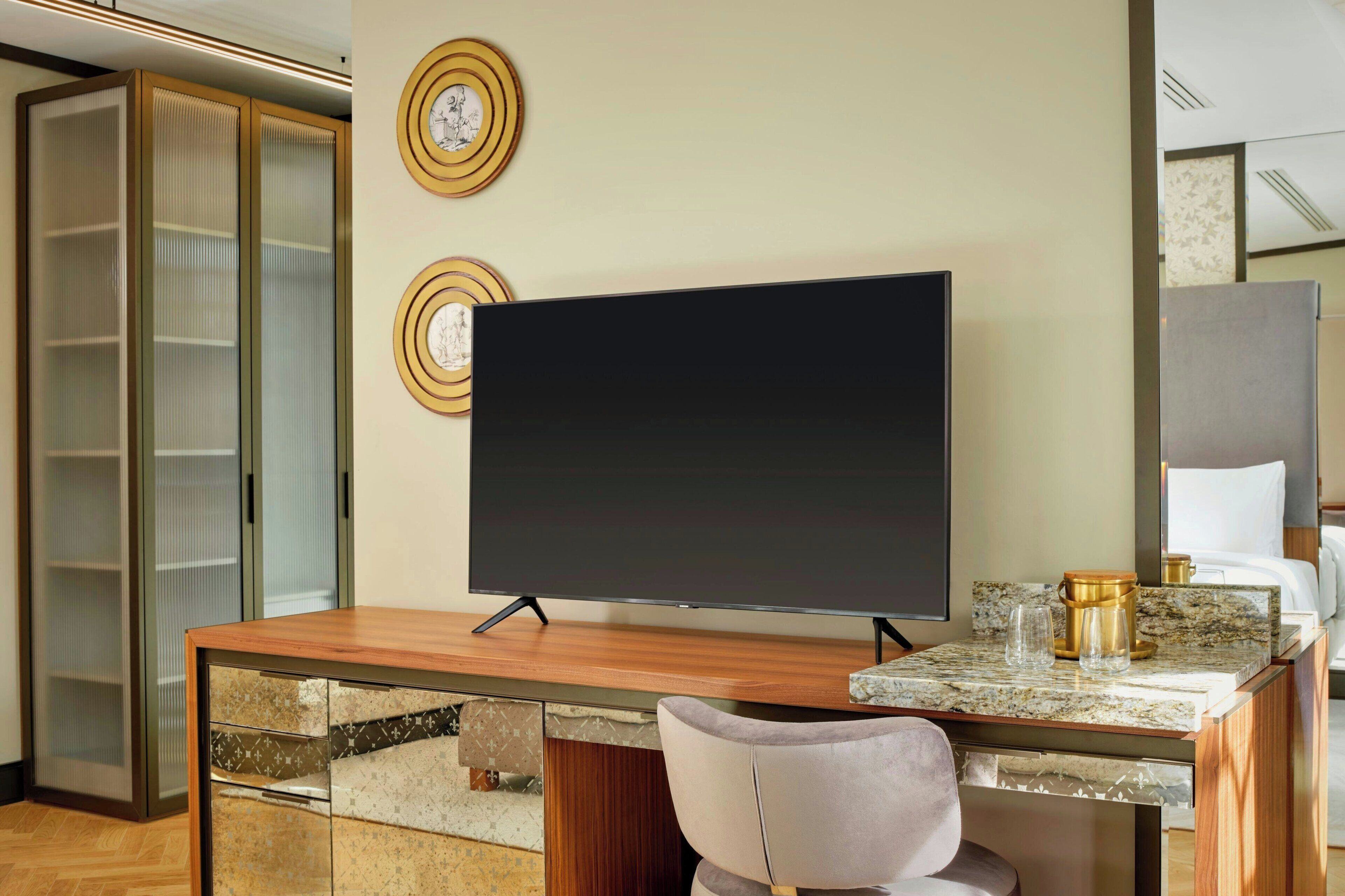 Une chambre d’hôtel avec un bureau en bois, un téléviseur à écran plat, un comptoir en marbre et une chaise.