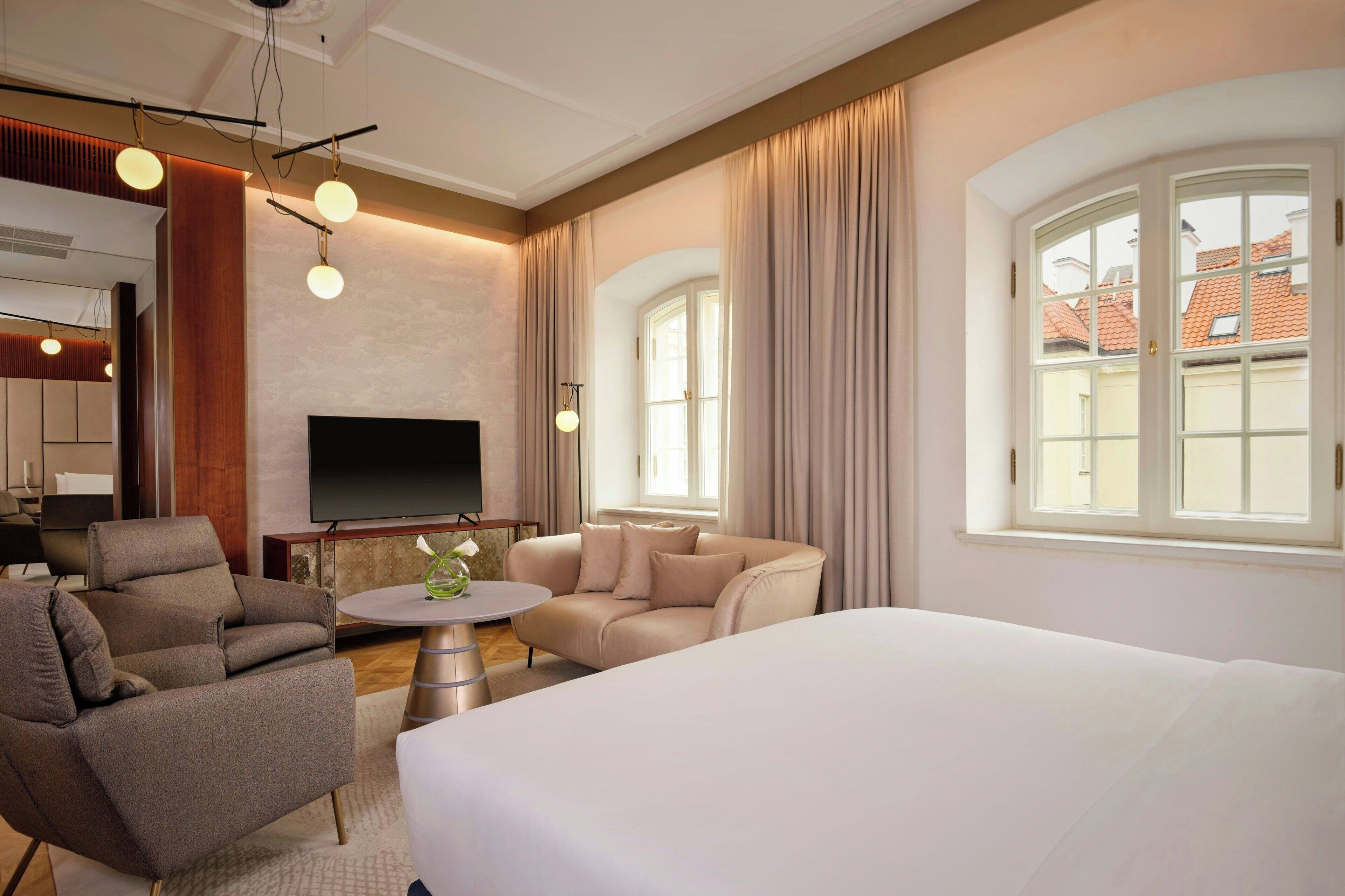 A hotel room with a large bed, two sofas, a TV, and a window with curtains.