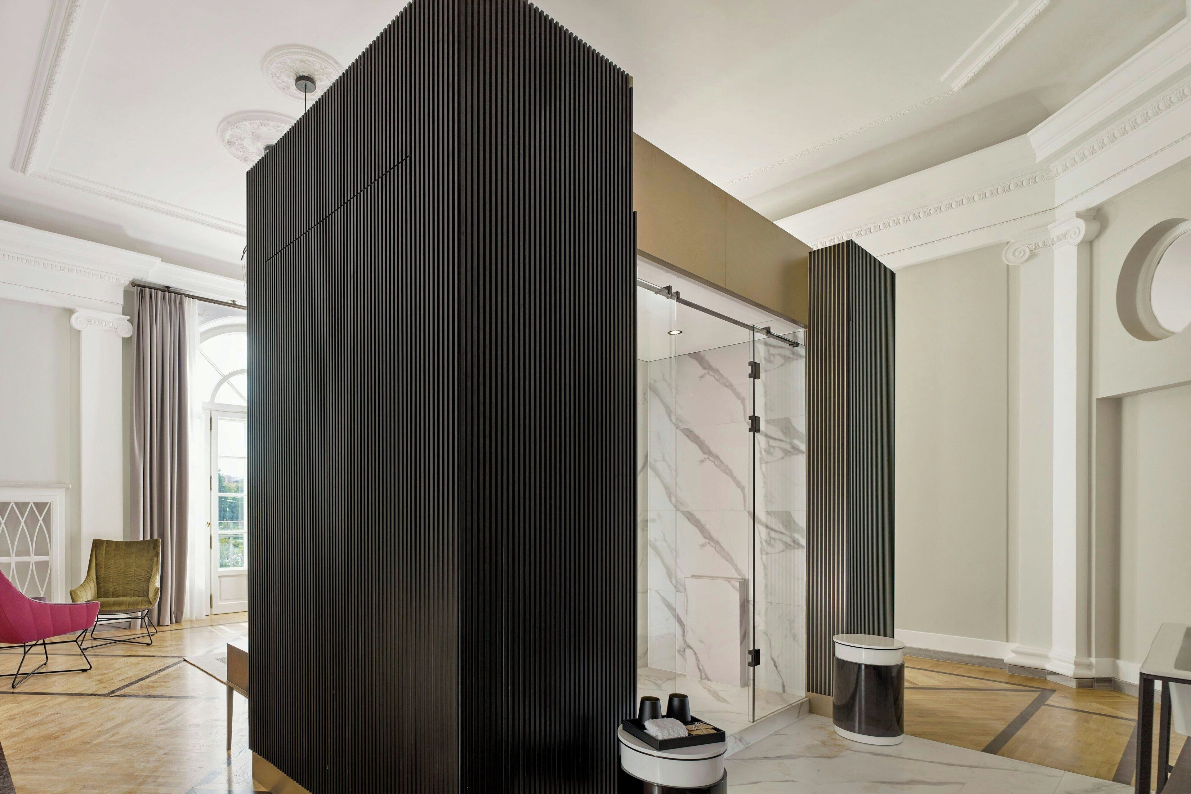 A modern hotel room with a large sliding door, a marble floor, a black partition, a glass shower, and a view of the outdoors.