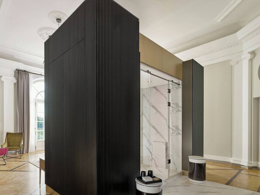 A modern hotel room with a large sliding door, a marble floor, a black partition, a glass shower, and a view of the outdoors.