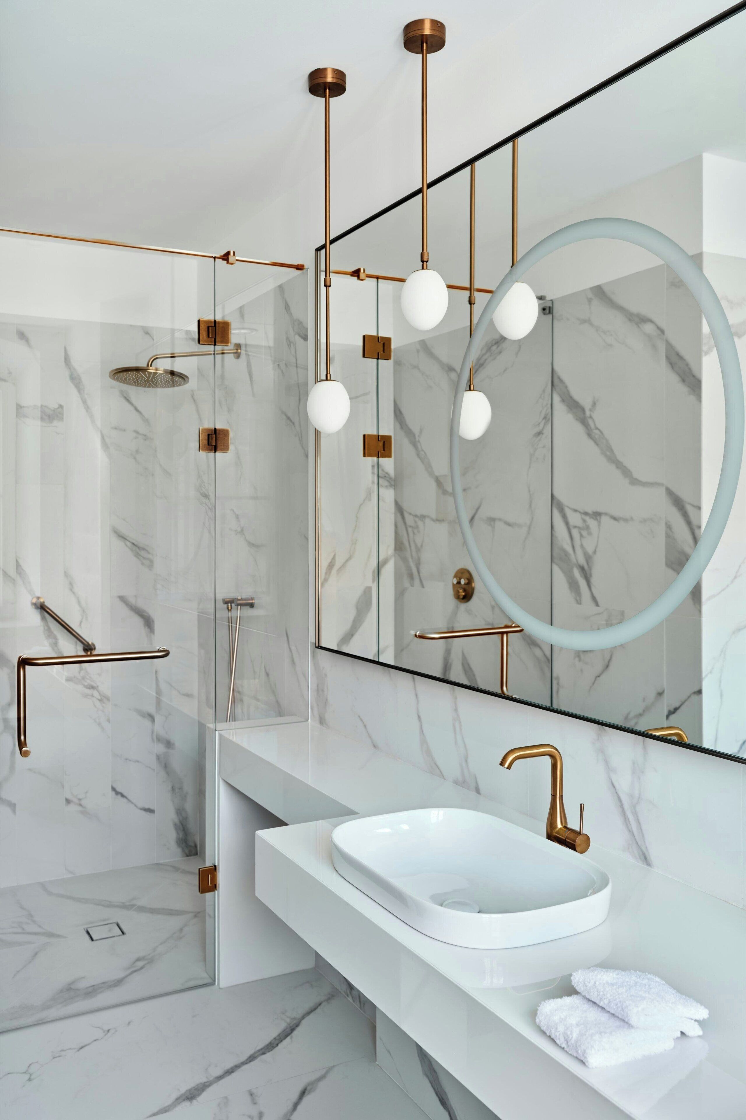 Un baño moderno con cabina de ducha de mármol, un lavabo blanco y un espejo grande.