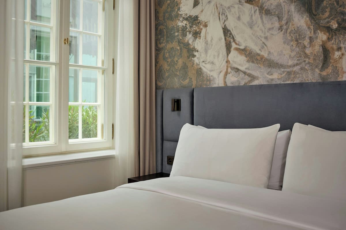A hotel room with a large bed, a window with curtains, and a textured wall.