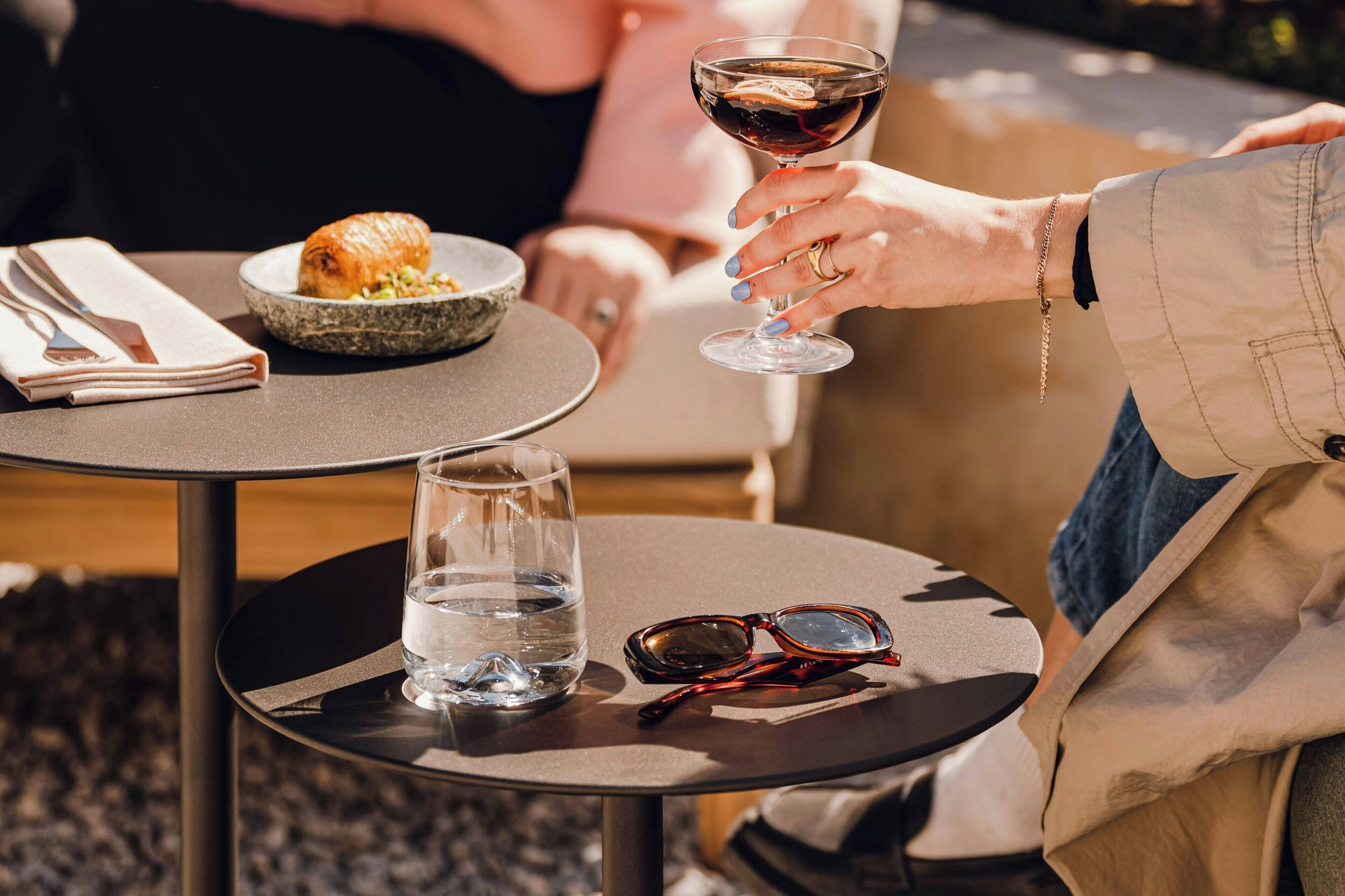 A dining table with a croissant, a bowl of salad, a glass of water, and a pair of sunglasses.