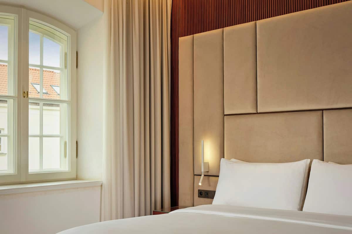 A hotel room with a large bed, a nightstand, a wall-mounted lamp, and a window with curtains.