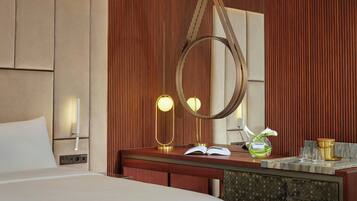 A hotel room with a bed, a wooden headboard, a bedside table with a lamp, a mirror, and a vase with flowers.