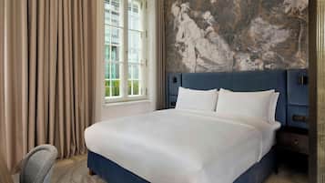 Ein Hotelzimmer mit einem großen Bett, einem Kopfteil, einem Fenster mit Vorhängen und einer Wand mit Wandgemälde.
