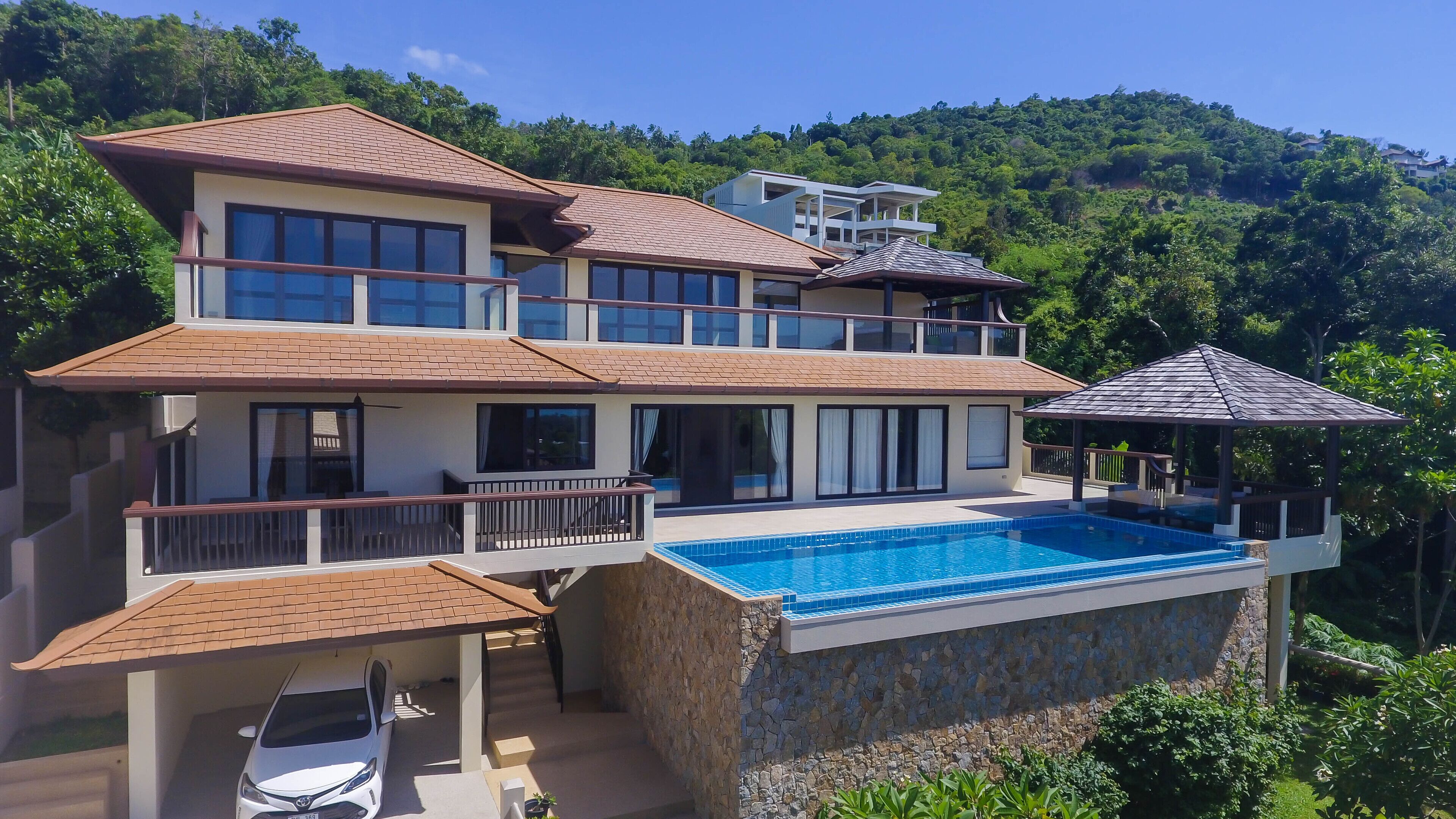 Una casa a più piani con piscina, un portico coperto e un'auto parcheggiata davanti.