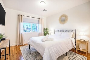 A neatly arranged bedroom with a bed, bedside tables, a television, and a window with curtains. - Modern • Tesla charger • 10 mins from Strip+Airport (Las Vegas)