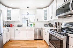A modern kitchen with white cabinets, stainless steel appliances, and a wooden floor. - Modern • EV charger • 10 mins from Strip+Airport (Las Vegas)