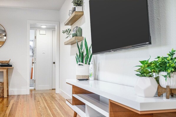 A modern living room with a flat-screen TV mounted on the wall, wooden flooring, and a white console table with decorative items.