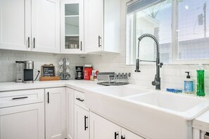 A kitchen with white cabinets, a stainless steel sink, a coffee maker, and a window with a view.