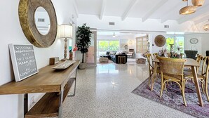 Un vaste espace de vie comprenant une table basse en bois, un grand miroir et un coin repas avec des chaises en osier.
